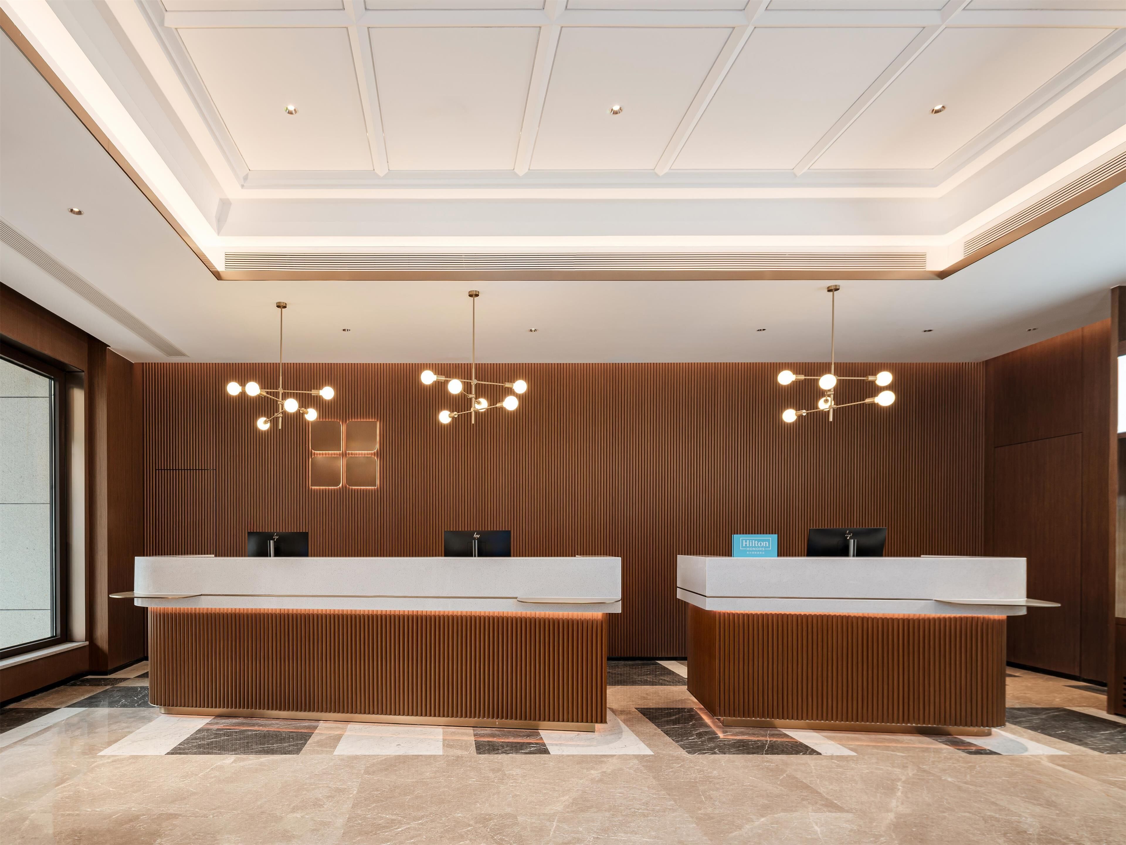 A hotel reception area with two reception desks, a modern ceiling design, and a wooden panel wall.