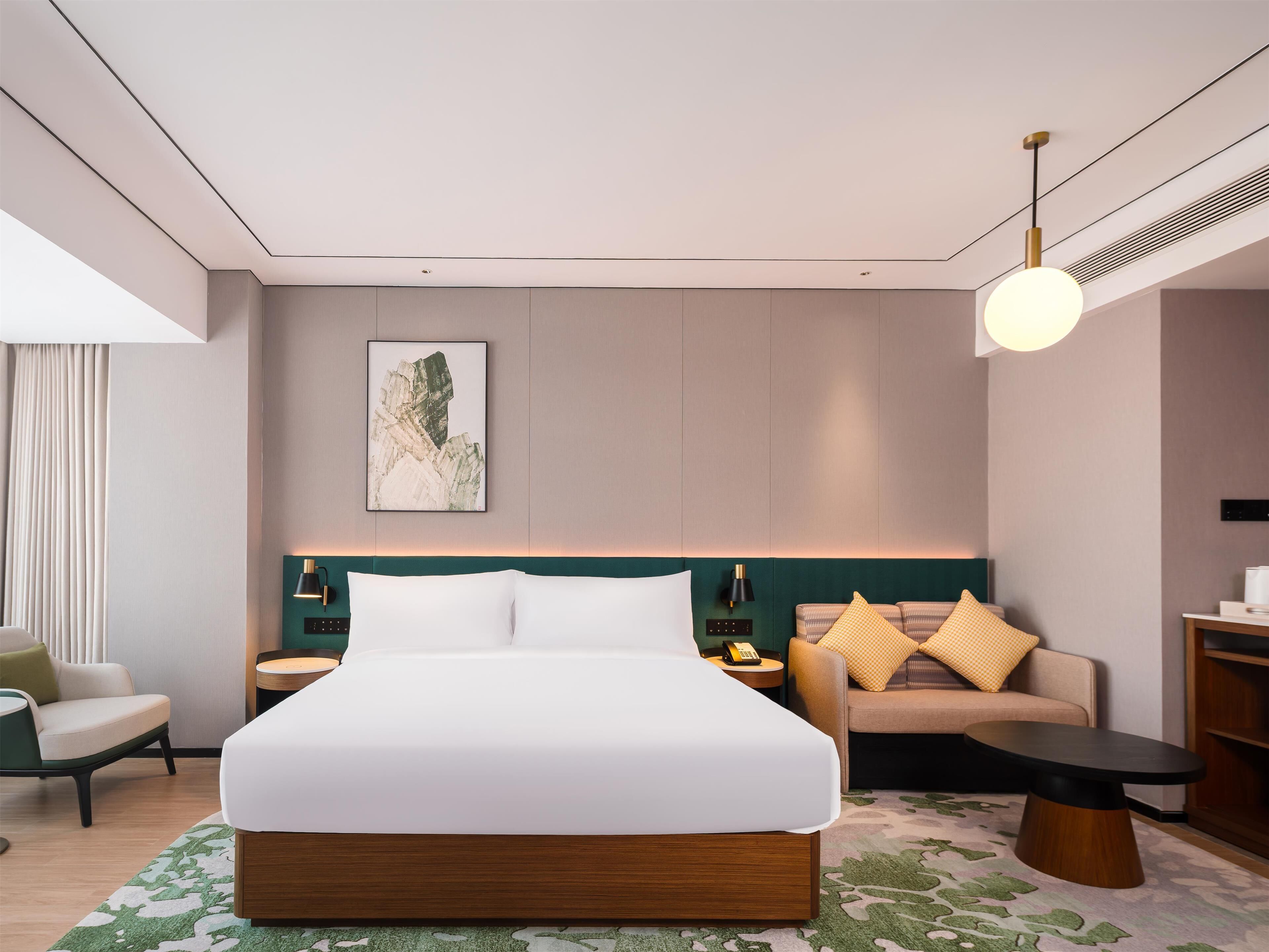 Een moderne hotelkamer met een groot bed, een bank, een tafeltje en een bureau. Er hangt een schilderij aan de muur en op het bureau staat een lamp.