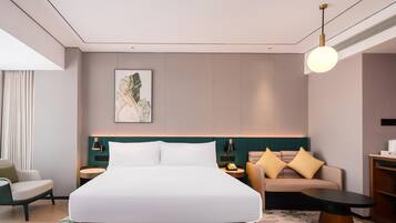 Een moderne hotelkamer met een groot bed, een bank, een tafeltje en een bureau. Er hangt een schilderij aan de muur en op het bureau staat een lamp.