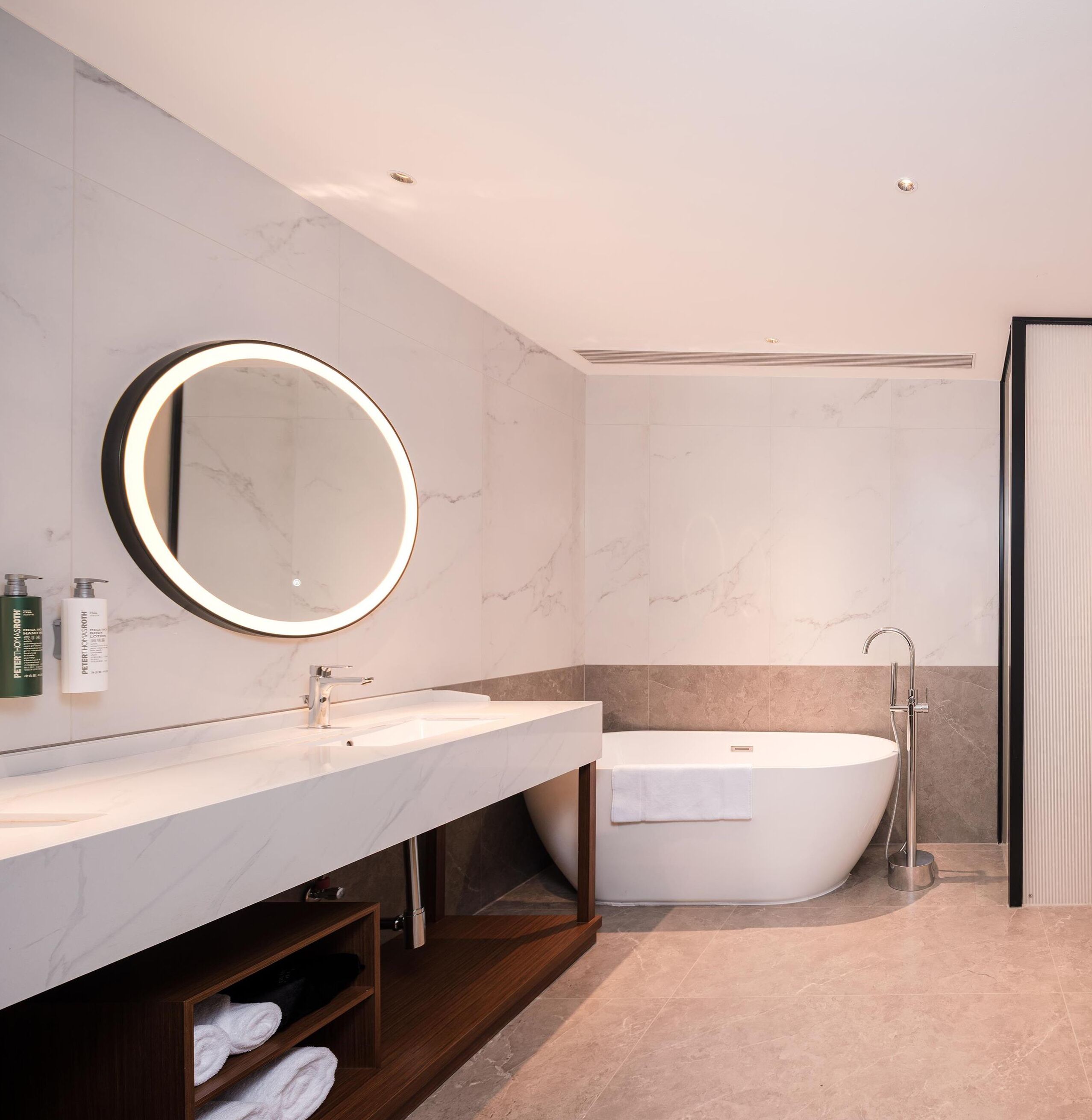 A modern bathroom with a marble vanity, a round mirror, a freestanding bathtub, and a shower.