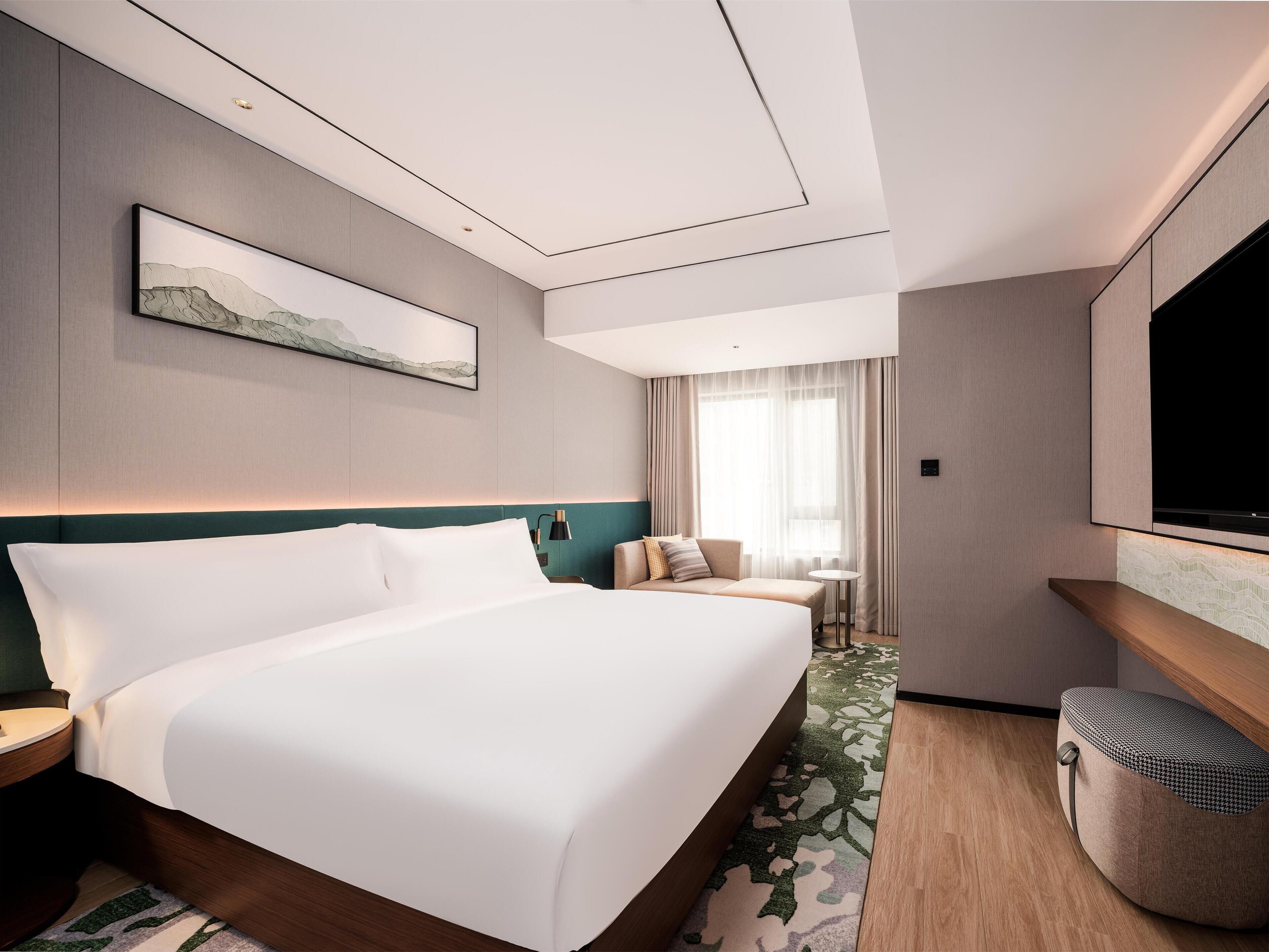A modern hotel room with a large bed, a seating area with a sofa and chairs, a small table, and a television mounted on the wall.