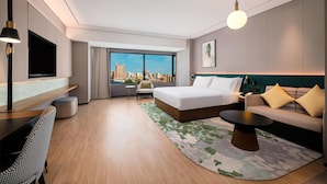 A modern hotel room with a large bed, a sofa, a TV, and a view of the city skyline. - Hilton Garden Inn Taiyuan Jiefang Road (Taiyuan)