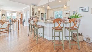 A spacious kitchen with wooden bar stools, pendant lighting, and a view of the dining area. - Spacious 4BR Home near Cape May Beach | Sleeps 10! (Cape May)