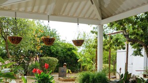A covered outdoor patio with a round table and benches, surrounded by potted plants and trees. - Cozy small studio room in Julianadorp with own bathroom and kitchenette (Willemstad)