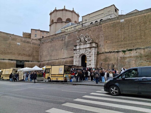 A historic building with an arched entrance, a bell tower, and a crowd of people in front. - Candia 66 at the Vatican Museums (Roma)