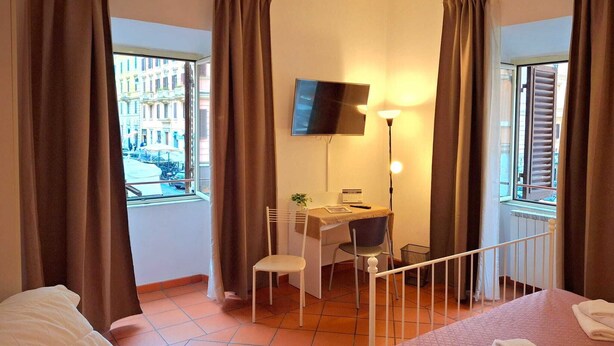 Une chambre d’hôtel avec un lit, un bureau et une chaise, une télévision et une fenêtre avec des rideaux.