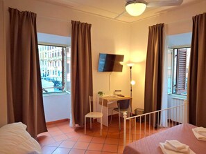 Ein Hotelzimmer mit Bett, Schreibtisch mit Stuhl, Fernseher und einem Fenster mit Vorhängen.