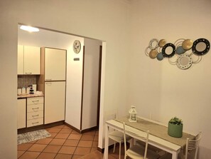 A compact kitchen with white cabinets, a tiled floor, and a dining area with a table and chairs. - Candia 66 at the Vatican Museums (Roma)