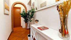 Un couloir avec un comptoir d’accueil blanc, une plante en pot, un vase contenant des fleurs séchées et une porte au fond.
