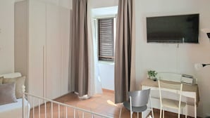 Une chambre avec un lit, un bureau, une chaise, une télévision et une fenêtre avec des rideaux.