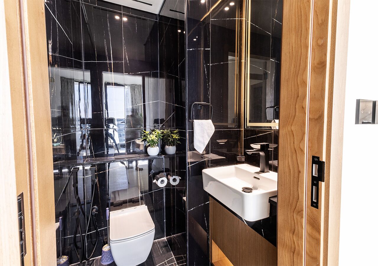 Un baño moderno con salpicadero de mármol negro, un lavabo blanco y un mueble de tocador de madera.