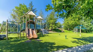 A playground with a slide and climbing structures, surrounded by green grass and trees. - Modern 3-bedroom Escape in Northwest Reno (Reno)