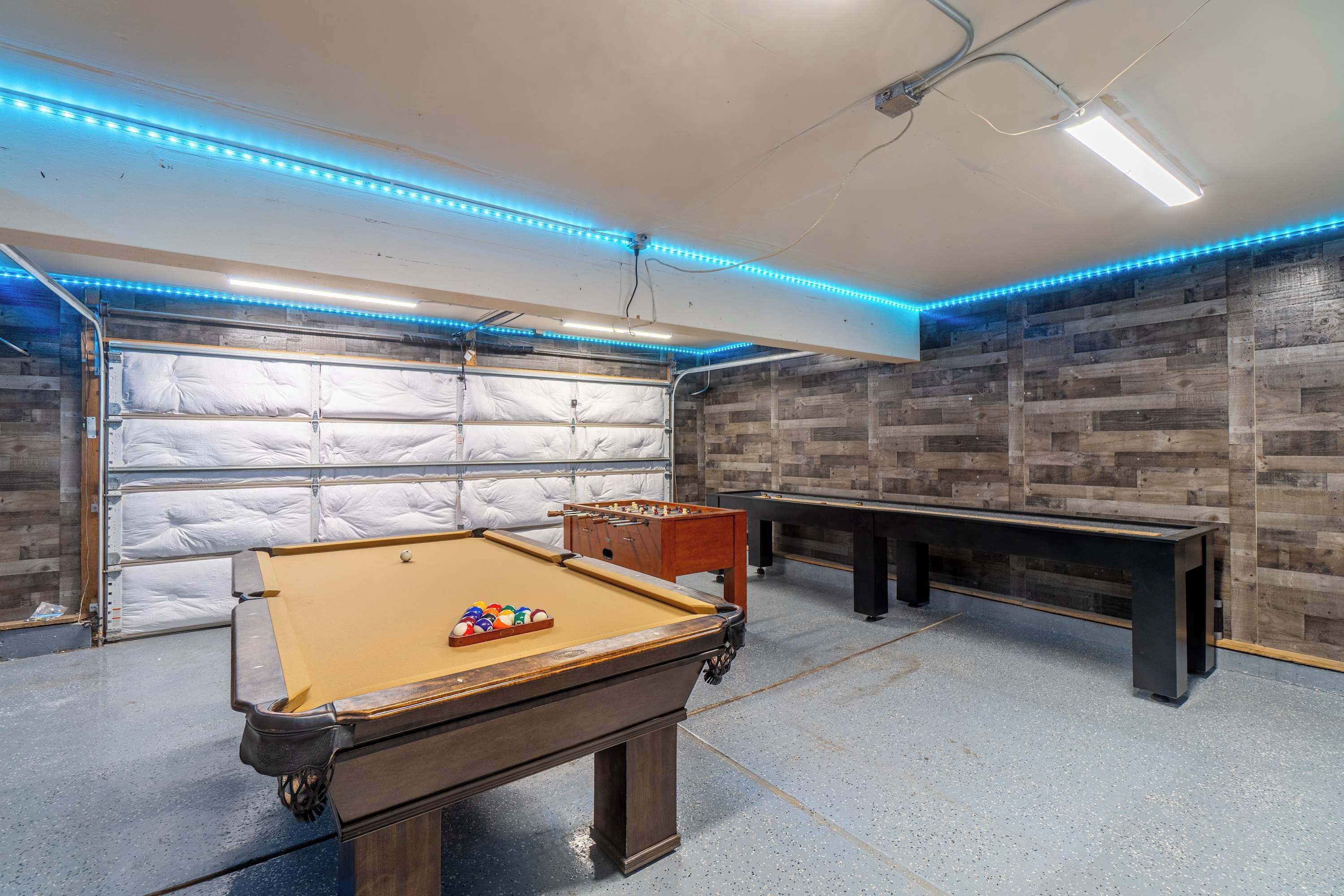 Ein Billardtisch, ein Kicker und ein Snookertisch in einem Raum mit Holzwänden und einer Garagentür.