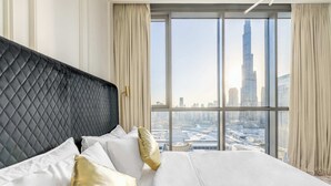 Habitación de hotel con una cama grande, cabecera negra y vistas a un paisaje urbano a través de amplias ventanas.