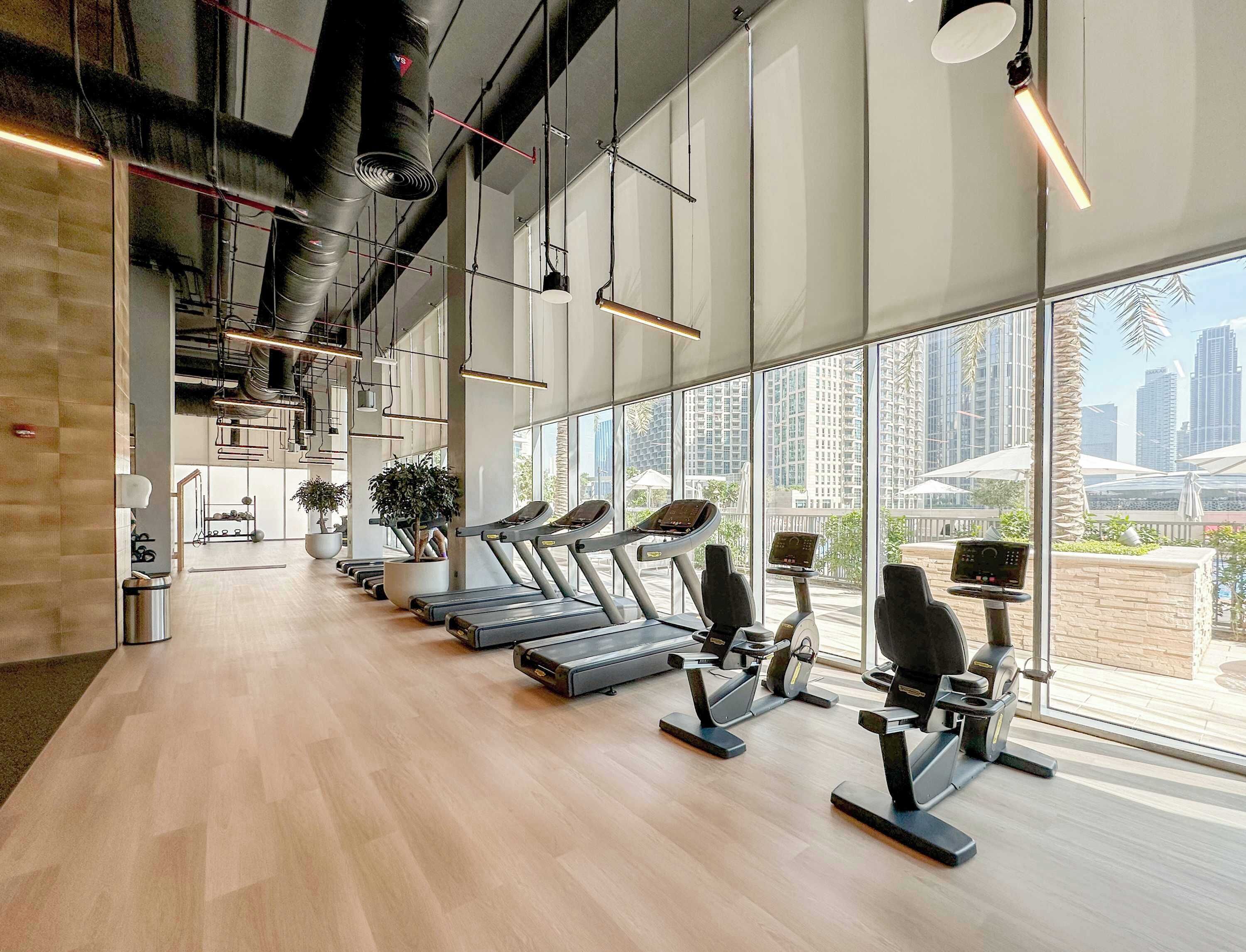 A modern gym with treadmills, stationary bikes, and a large window with a city view.
