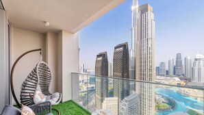 Un balcó amb una cadira penjant, una taula petita i una vista d'un paisatge urbà amb edificis alts i un riu.