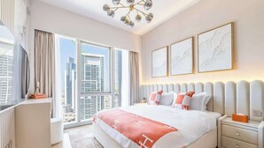 A modern hotel room with a large bed, a bedside table, a nightstand, and a view of the cityscape through large windows.