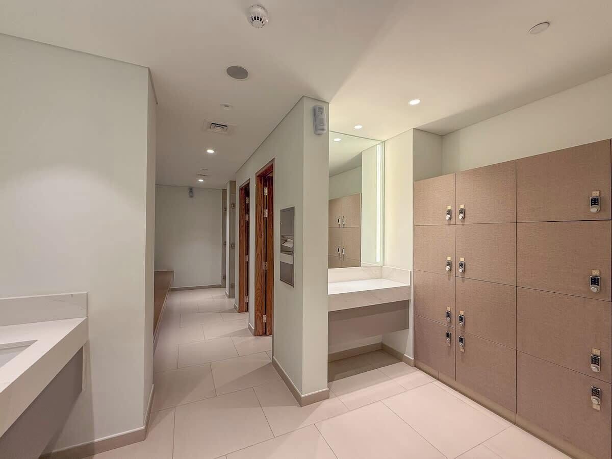 A modern hotel corridor with a long hallway, a large mirror, and a row of lockers on one side.