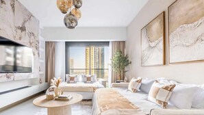 Een moderne hotelkamer met een groot bed, een bank, een salontafel en een televisie. Er zijn grote ramen met uitzicht op de stad.