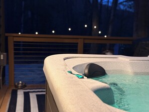 A hot tub on a wooden deck with a railing, surrounded by trees.