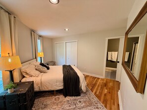 A bedroom with a bed, a bedside lamp, a suitcase, a mirror, and a wardrobe.