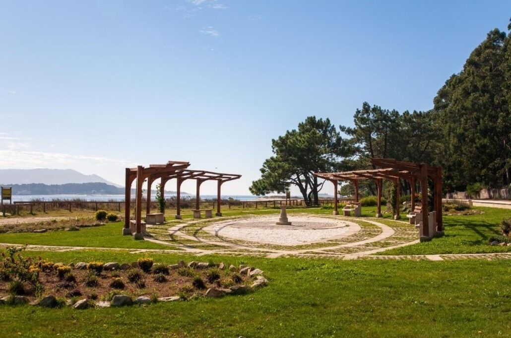 Un parc agrémenté de pergolas en bois, doté d’un espace circulaire central et offrant une vue sur la mer et les montagnes en arrière-plan.