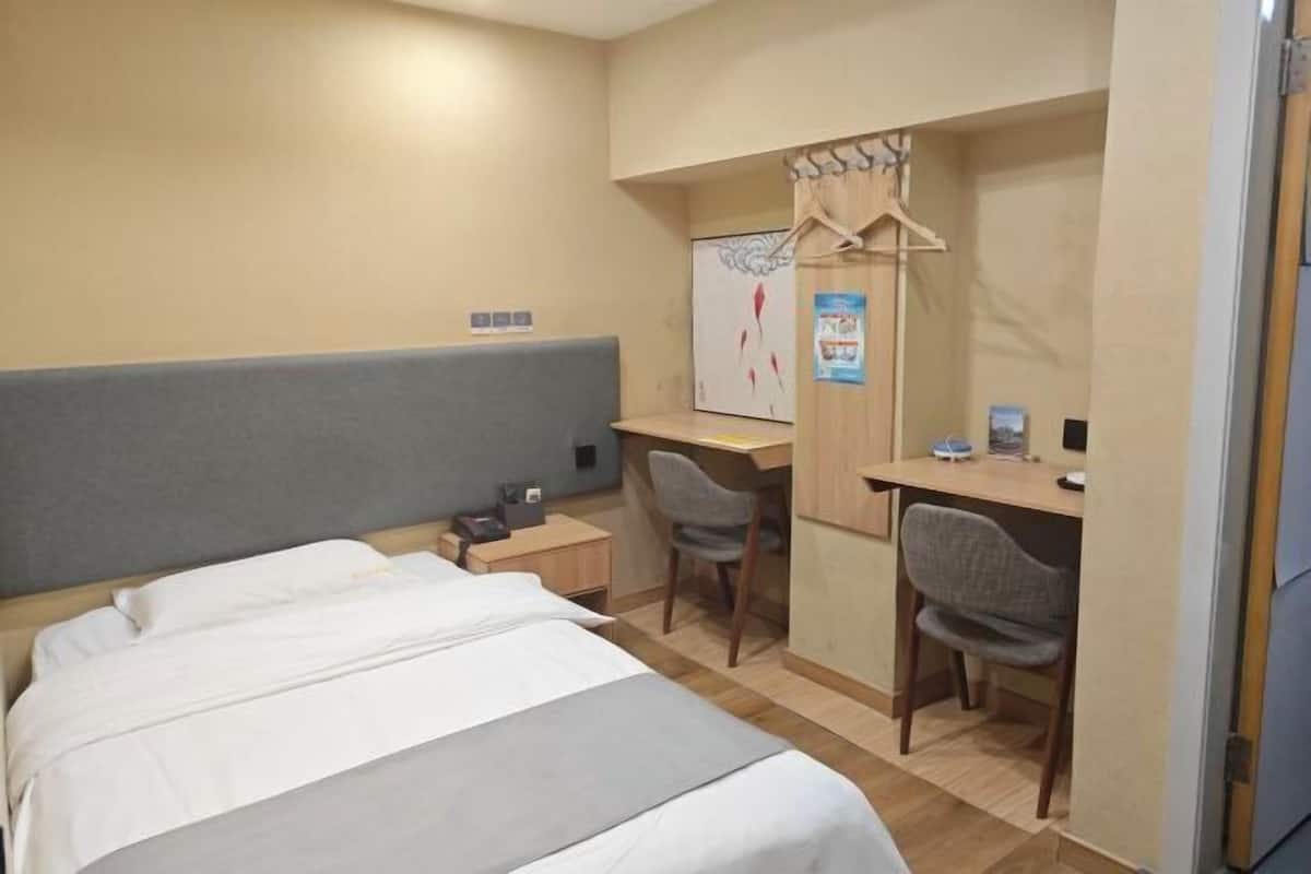 A hotel room with a bed, a desk, two chairs, a wardrobe, and a poster on the wall.
