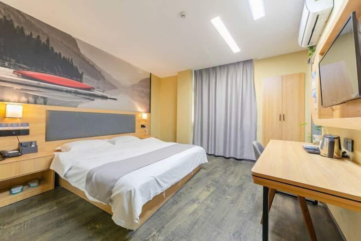 A hotel room with a bed, a desk, a TV, and a painting on the wall.