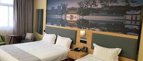 A hotel room with two beds, a cityscape mural, a nightstand with a phone, and a window with curtains.