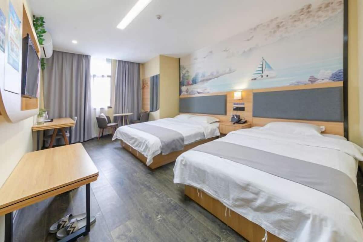 A hotel room with two beds, a desk, and a chair. There is a painting on the wall and a window with curtains.