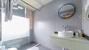 A modern bathroom with a toilet, a sink with a mirror above it, and a glass shower enclosure. - Yi An Hotel (Suzhou)