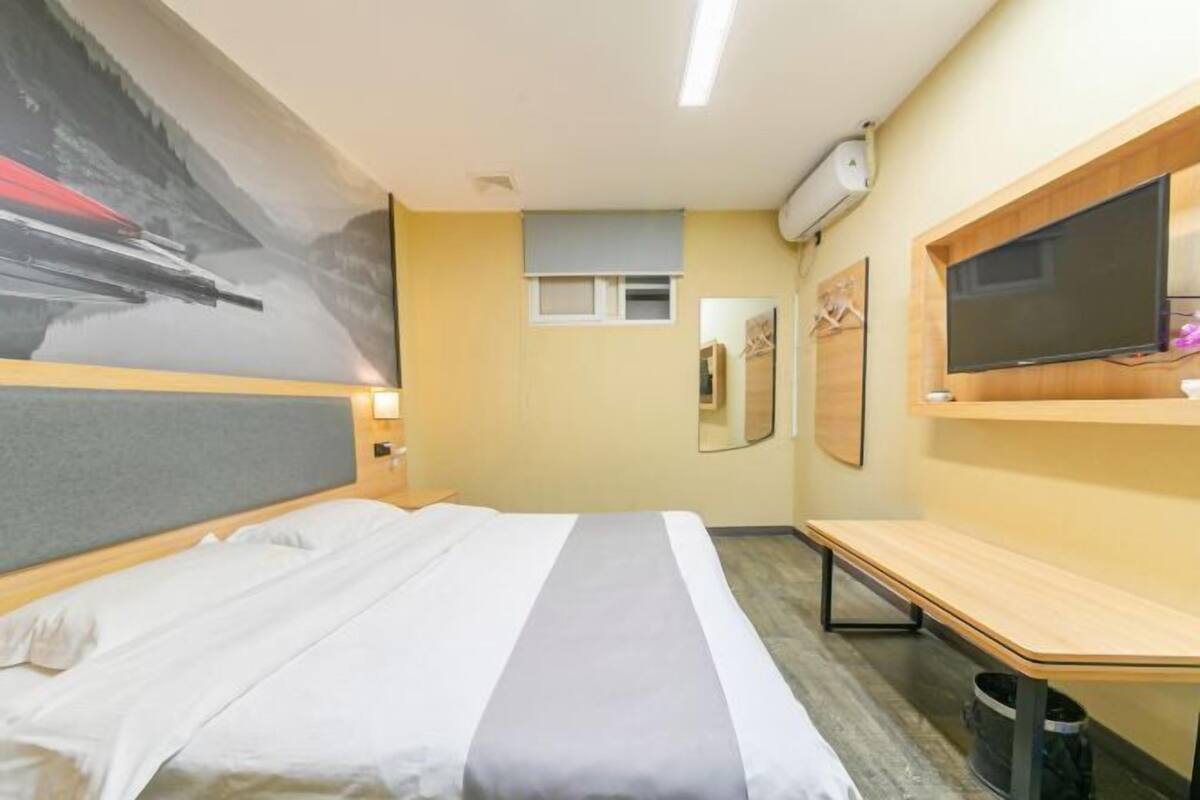 A hotel room with a bed, a desk, a television, and a large painting on the wall.