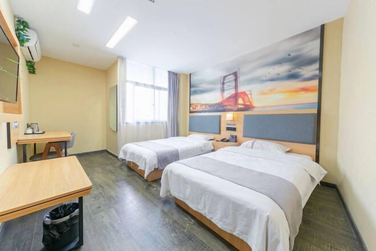 A hotel room with two beds, a desk, and a trash bin.