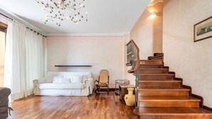 Un ampio soggiorno con una scala in legno, un divano bianco e un lampadario.