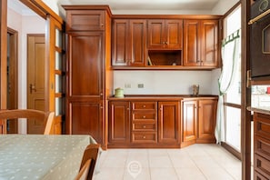 A kitchen with wooden cabinets, a dining table, and a window with curtains. - Casa Daniela - Pula Dream (Pula)