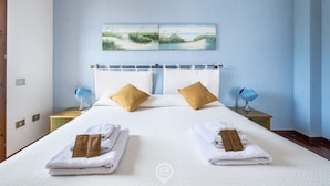 Una camera d'albergo con un letto grande, due cuscini, un comodino con una lampada e un quadro appeso al muro.
