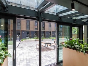 A modern building with a glass entrance, outdoor seating, and a courtyard. - Student Only The Refinery (Leeds)