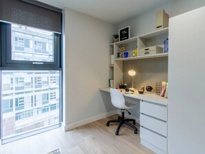A modern office space with a desk, chair, shelves, and a window with a city view. - Student Only The Refinery (Leeds)