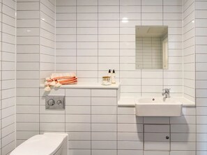 A modern bathroom with white tiles, a toilet, a sink, and a mirror. - Student Only Gulson Gardens (Coventry)