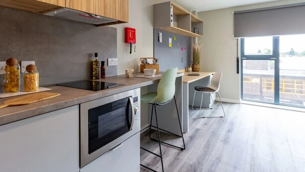 Eine moderne Küche mit Einbauofen, Mikrowelle und einer Holzausziehtischplatte. Zwei Stühle und ein kleiner Tisch mit einer Pflanze sind ebenfalls vorhanden.