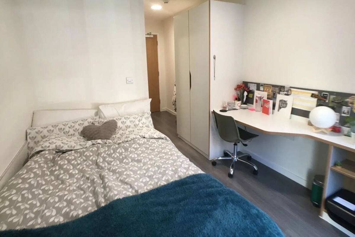 A bedroom with a bed, a desk, and a wardrobe.