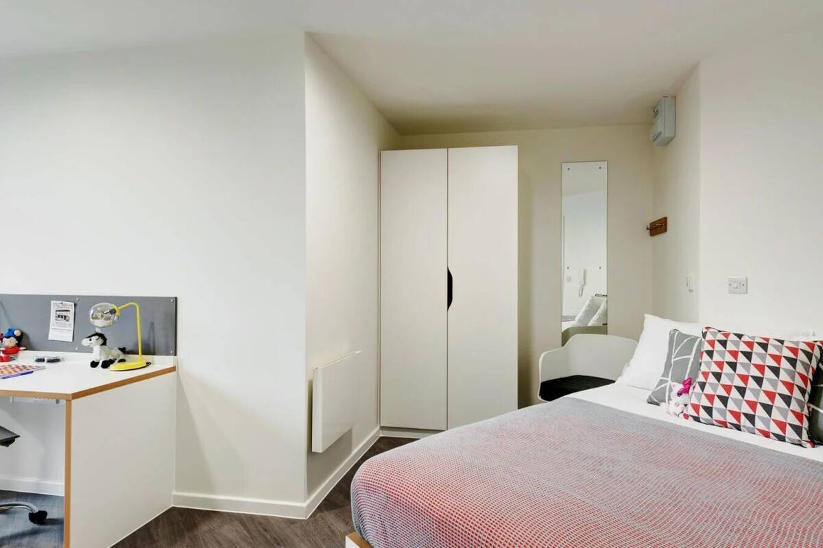 A compact bedroom with a bed, a desk, and a wardrobe.
