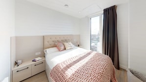 Ein modernes Hotelzimmer mit einem großen Bett, einem Nachttisch, einer Fensterbank und Blick auf die Stadt durch ein großes Fenster.