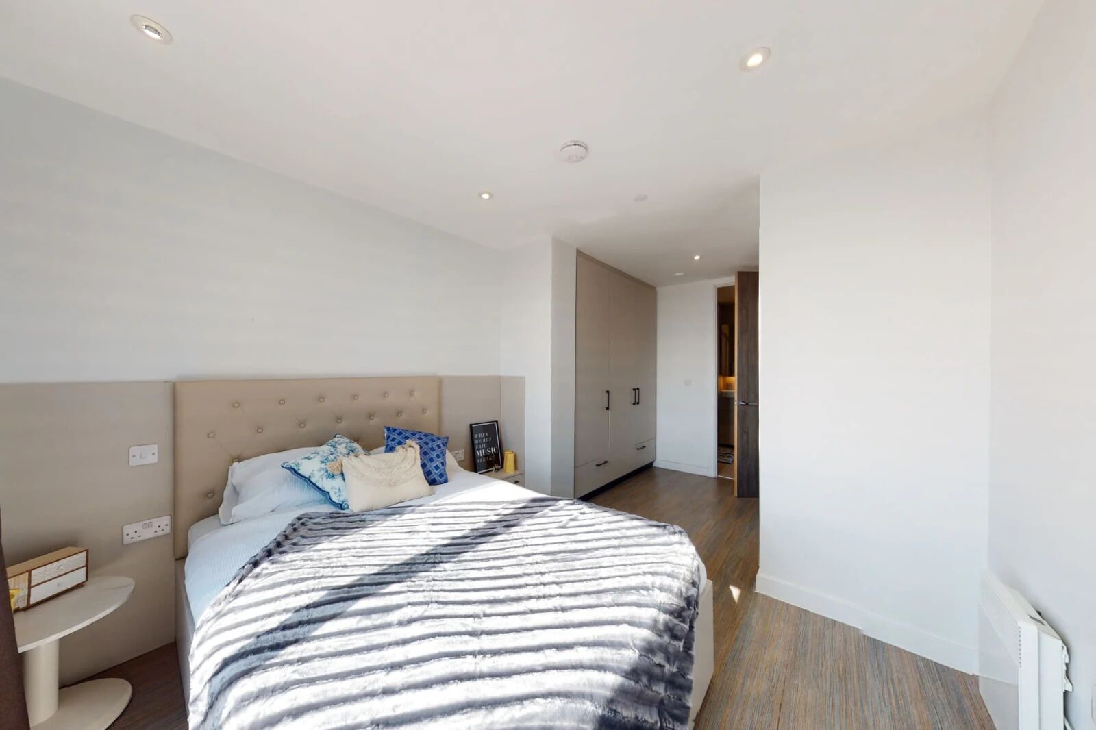 A modern bedroom with a large bed, a bedside table, and a wardrobe.