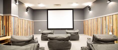 Un salón de conferencias con una pantalla grande, sillones tipo bean bag grises y paredes con listones de madera.