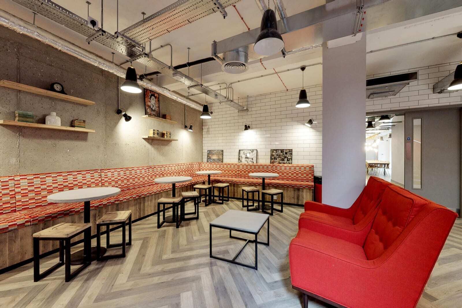 A modern cafe with a red and white checkered bench, multiple tables, and a red sofa.