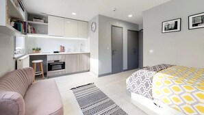 A modern bedroom with a bed, a desk, and a kitchenette. - For Students Only Abodus The Walls Southampton - Campus Accommodation (Southampton)