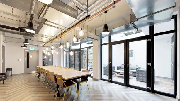 A conference room with a long table, chairs, pendant lighting, and large windows offering views of outdoor seating. - For Students Only Abodus The Walls Southampton - Campus Accommodation (Southampton)