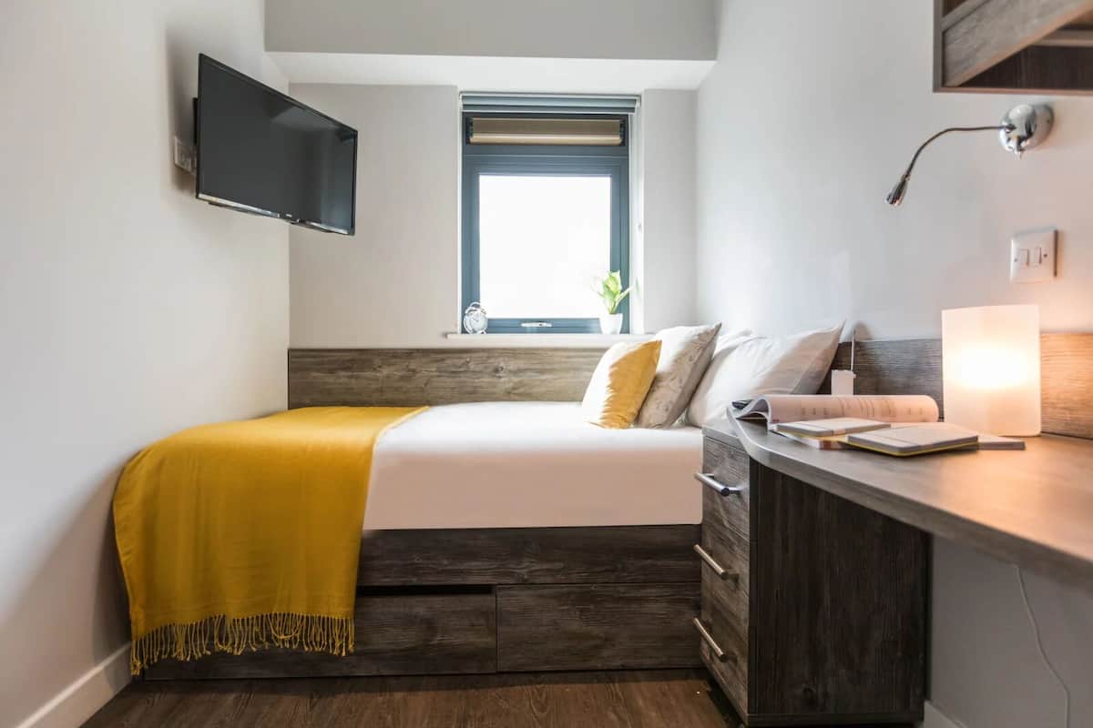 Une chambre à coucher comprenant un lit, une table de chevet, une lampe et un téléviseur fixé au mur.