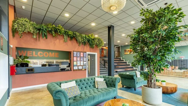 A reception area with a 'WELCOME' sign, a green sofa, a coffee table, and a large potted plant. - Student Only Radford Mill (Nottingham)